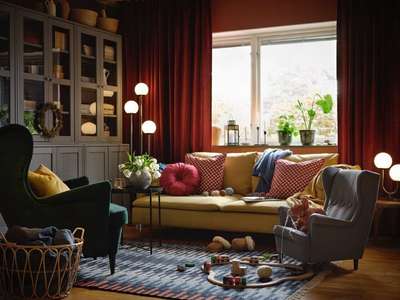 Create a comfortable living room with a black and white colour scheme, an off-white couch with two red pillows, long beige and brown drapes, and shelves brimming with books, lamps, and figurines. #interior  #decor  #ideas  #home  #interiordesign  #indian  #colourful #decorshopping