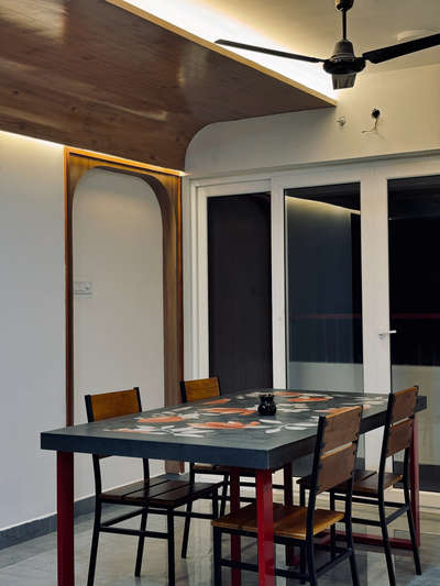 Project type: Interior design and Execution
Location: Pangappara, trivandrum
The Red Thread-
This residential interior project harmoniously blends industrial strength with tropical calm, centered around a unique visual element — red steel bars that subtly connect every custom-built furniture piece. The bold red becomes the common thread weaving through a cohesive narrative of design, linking the sofa, dining table, TV unit, and storage systems into a singular visual language.
Natural textures like walnut wood laminates, botanical graphic wall panels, and ceramic printed dining surfaces contrast beautifully with the industrial robustness of steel, softening the palette with warm beige upholstery and intricate tilework at the wash zone.
Architectural details such as curved wood-clad ceilings, arched niches, and ambient lighting elevate the spatial experience while maintaining minimalism and clarity in function. The space seamlessly balances artistry with utility, presenting a bold, modern yet nature-inspired aesthetic  #KitchenInterior #homeimprovement  #homeinterior  #LivingRoomTable  #LivingroomDesigns #KitchenInterior  #minimalistichome