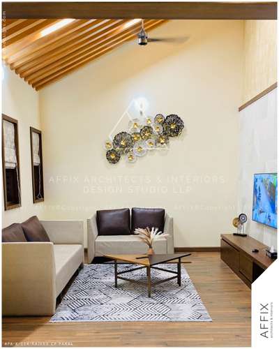 This living area blends natural warmth with modern elegance, featuring wood-finished flooring and a sloped ceiling accented by wooden purlins. Small side windows allow soft, diffused light to brighten the space, highlighting the cozy neutral-toned seating arrangement. The artistic wall décor adds a touch of sophistication. Minimalist elements like the wall-mounted TV and sleek console maintain a clean, uncluttered look, creating a serene and inviting atmosphere. #Architect  #architecturedesigns  #Architectural&Interior  #architectsinkerala  #architecturedaily  #architecture_hunter  #best_architect