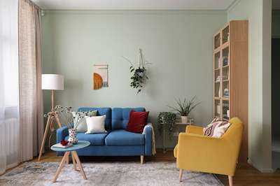 Create a cheerful and uplifting look with a celebration of colour in your living room. Use a handwoven wall decor and a decorative vase on the coffee table to add artistic touches to the room, whilst a hanging plant introduces a botanical element. A colourful assortment of red, green, and white throw pillows make playful contrast with the blue modern sofa and the blue coffee table design. #interior #decor #ideas #home #interiordesign #indian #colourful #decorshopping