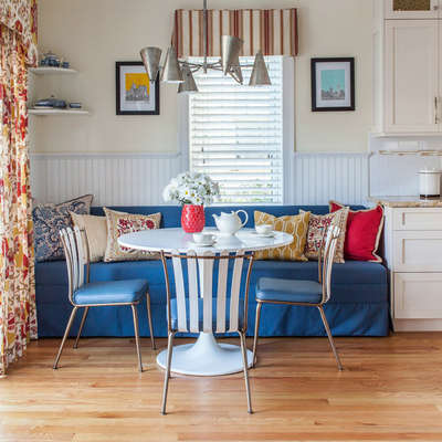 Get this boho-style dining room with transitional medium-tone wood floors and beige walls. Invest in a round dining table along with designer chairs and a sofa with printed cushions. Use floral print curtains and flower vases to get a warm and appealing look.  #interior  #decor  #ideas  #home  #interiordesign  #indian  #colourful #decorshopping