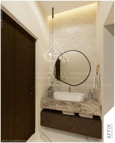 The wash area features a natural pebble-tiled wall highlighted by cove lighting, contrasting with a veined marble countertop over a dark wood chevron cabinet, centered by a round black mirror and a minimalist hanging light fixture. LED strip lights above the pebble wall to create a soft, upward glow, making the texture pop and providing a warm, moody halo that frames the mirror and basin area beautifully. #Architect  #architecturedesigns  #Architectural&Interior  #architecturekerala  #best_architect  #archituredesign