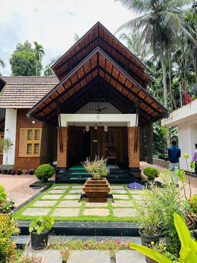 The 1800 sqft residential building is designed with a traditional tropical theme, featuring laterite stone cladding on the facade. It includes three bedrooms, each with attached toilets for added convenience. To enhance natural lighting, skylights have been incorporated into the design, allowing sunlight to filter into the living spaces. This combination of traditional aesthetics and modern functionality creates a unique and inviting living space.