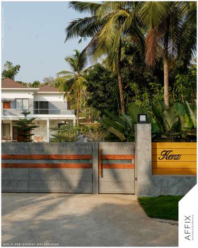 Opening to the heart of the landscape, this gate seamlessly blends with its natural surroundings. Crafted from sturdy metal sheets, adorned with intricate CNC cutwork, and accented with warm wooden paneling, it exudes modern elegance. The imported texture paint adds a vibrant touch, while the surrounding plants and trees breathe life into the scenery. Tall coconut trees, lush calathea leaves, and ornamental shrubs frame the view, creating a serene escape that invites you to step into a world of breathtaking beauty and tranquility. #Architect  #architecturedesigns  #Architectural&Interior  #kerala_architecture  #best_architect