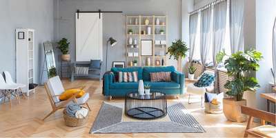 Get this bright and cheerful living space with light grey walls, wooden floors and some wooden made furnitures. The room has a large window that lets in natural light and is furnished with a blue couch, a round coffee table, black floor lamp and different shaped vases .#interior #decor #ideas #home #interiordesign #indian #colourful#decorshopping